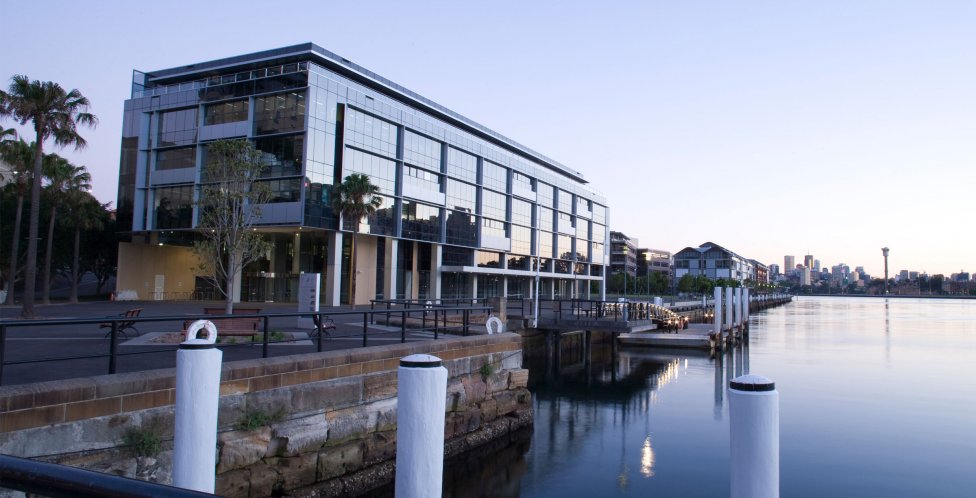 Waterfront glass building with city skyline and palm trees Modern glass building by waterfront promenade with palm trees and city skyline at dusk.